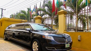 A black SUV parked in front of a yellow building with a gated entrance. - Banex Hotel and Suites (Lagos)