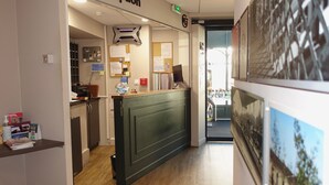 A reception area with a reception desk, a bulletin board, a computer, and a door leading to another room. - Hôtel de la Gare (La Roche-sur-Yon)