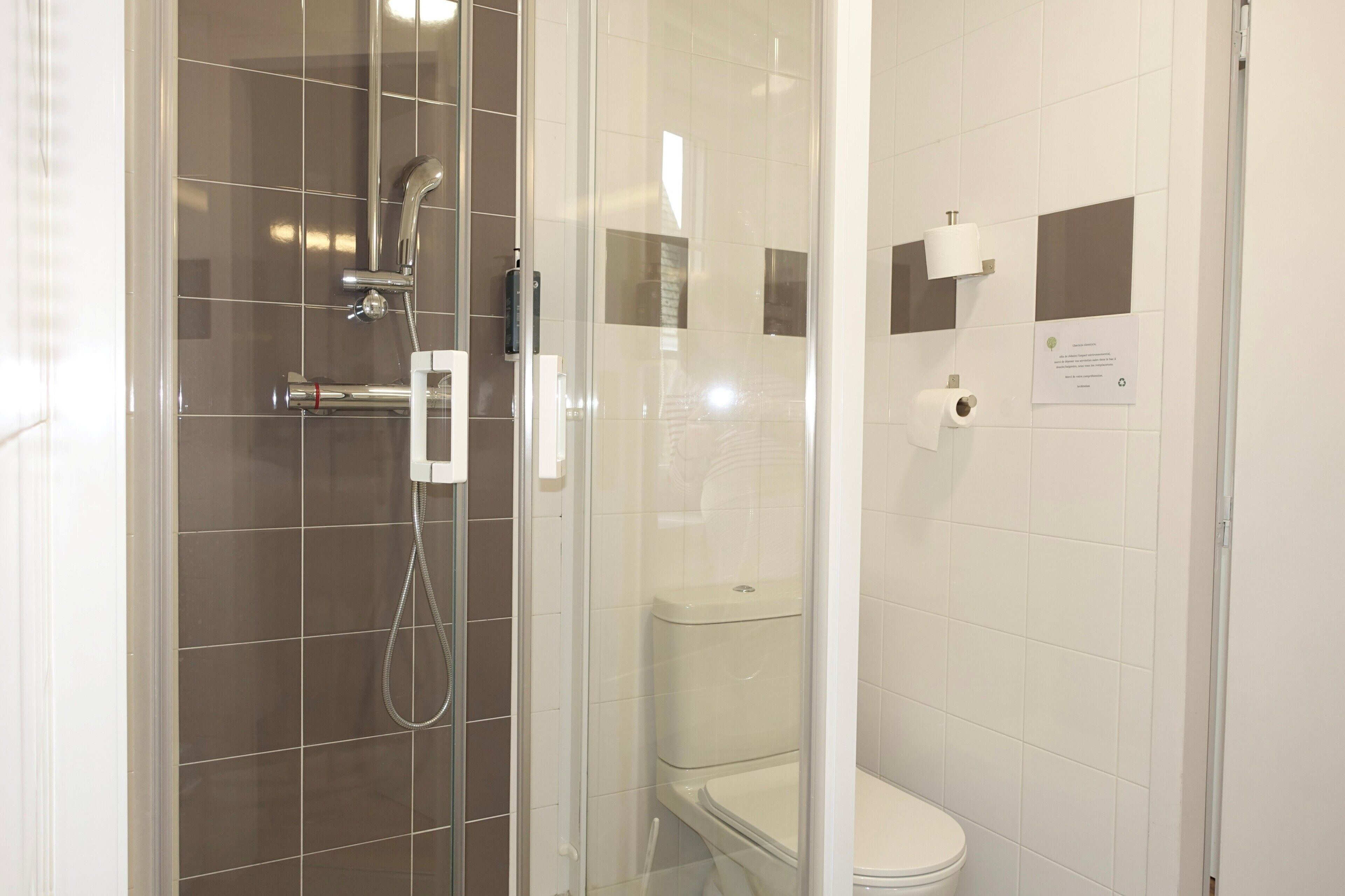 A modern bathroom with a glass-enclosed shower, a toilet, and a hand dryer.
