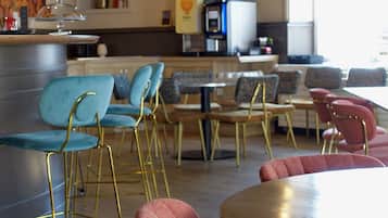 A restaurant with round tables and chairs, a kitchen area, and a television mounted on the wall.
