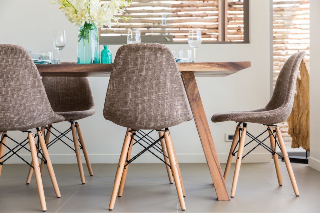 A dining area with four brown chairs and a wooden table, set against a backdrop of a wooden slatted wall and a window.