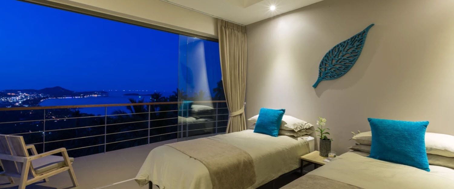A hotel room with two beds, a large window with a city view, and a balcony with a chair.