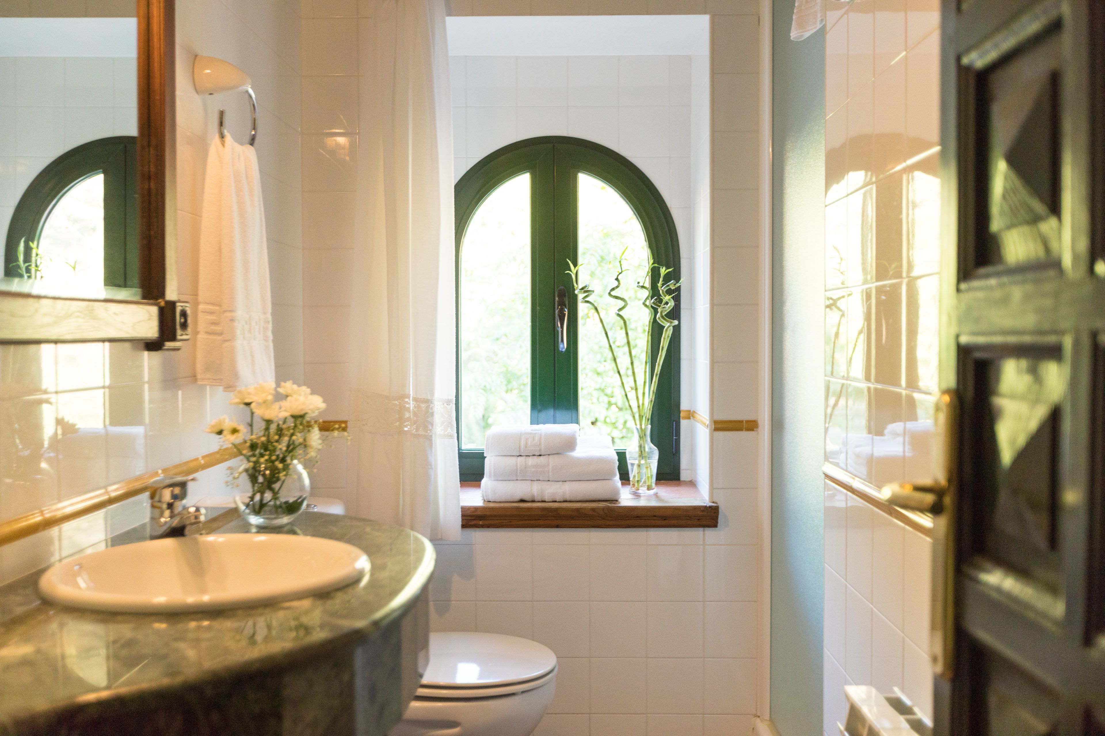 A bathroom with a marble sink, a toilet, and a window with a view of greenery.