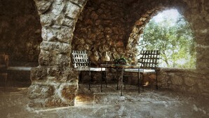 An outdoor stone archway with a table and chairs, surrounded by stone walls and a view of trees. - Calerilla Hotel (La Iruela)