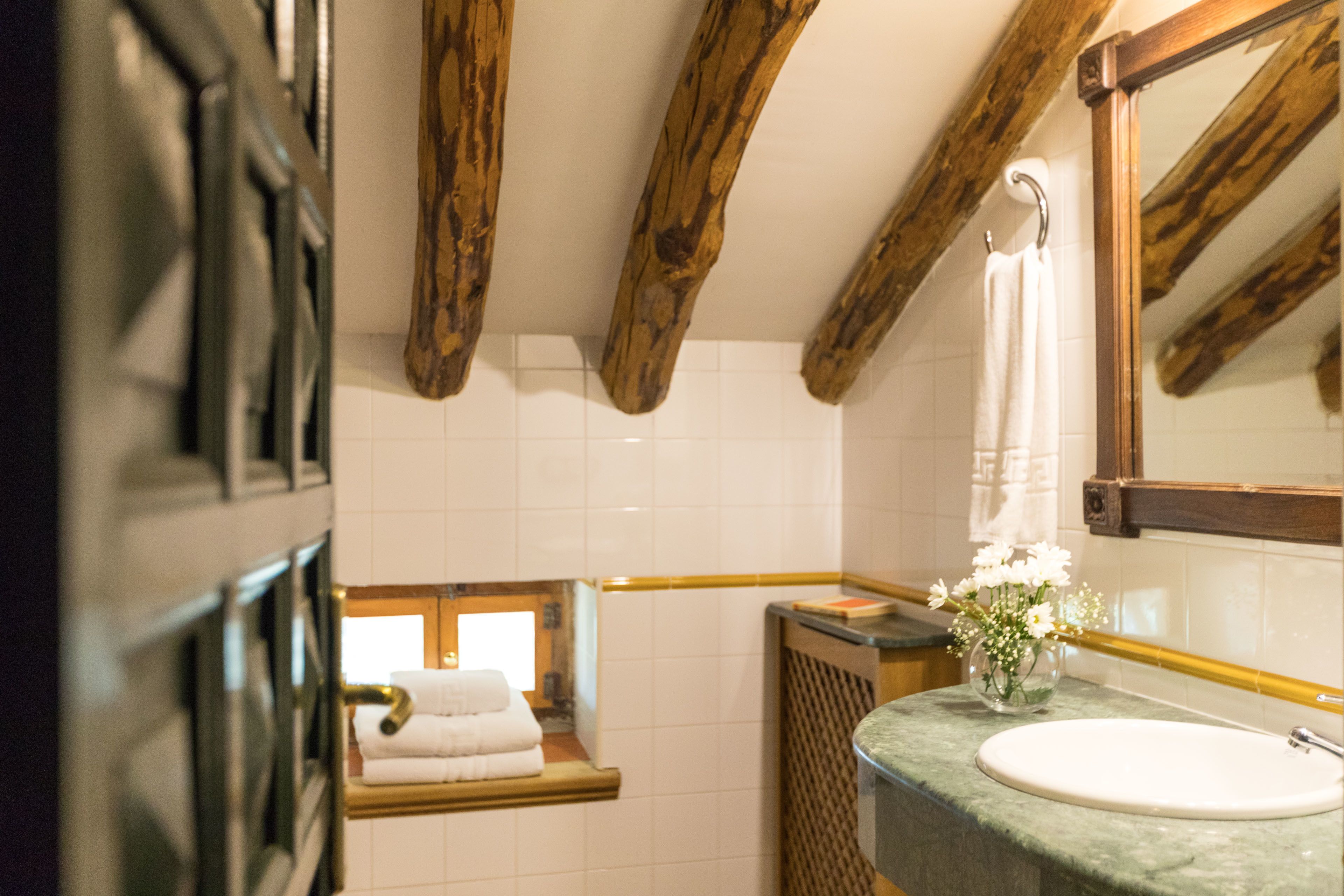 Un baño con techo de madera, una ventana, un lavabo con un florero y un perchero para toallas.