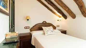 Un dormitorio con cabecera de madera, cama con almohada estampada, lámparas de noche, mesita de noche con libros y un cuadro en la pared.