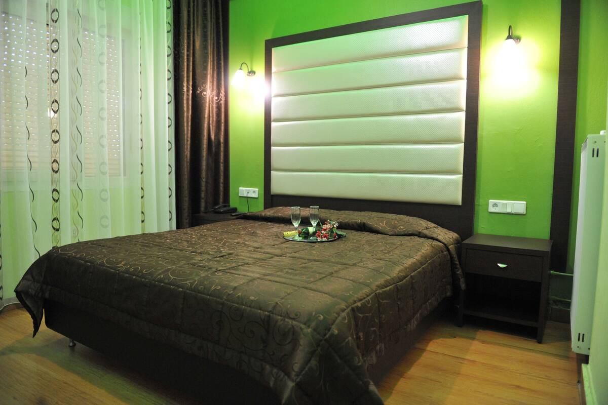 Ein Schlafzimmer mit einem großen Bett, zwei Nachttischen, einer Ablagefläche, einer Wandleuchte und einer Steckdose.