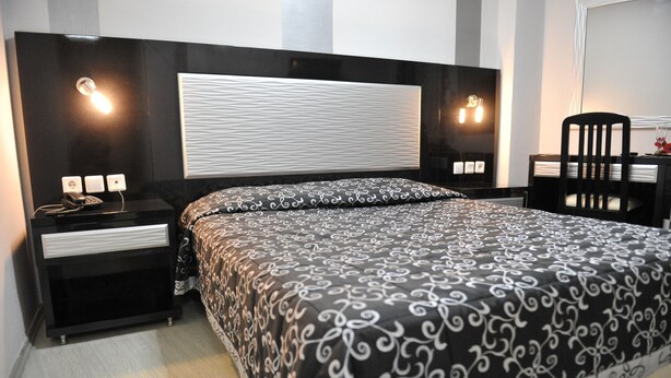 A modern bedroom with a large bed, a bedside table with a lamp, and a chair. - Hotel Emporiko (Drama)