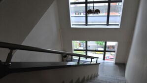 A staircase with a metal handrail leading to a landing with large windows. - Hotel Emporiko (Drama)