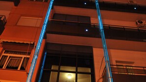 A building with a prominent vertical blue light feature and a sign indicating a hotel. - Hotel Emporiko (Drama)