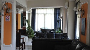 A living room with a black leather sofa, a wooden coffee table, and a dining area with a table and chairs. - Hotel Emporiko (Drama)