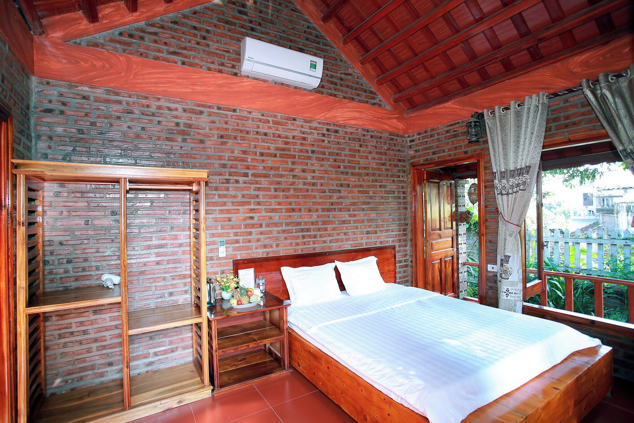A room with a brick wall, a wooden bed, a nightstand, and a window with curtains.