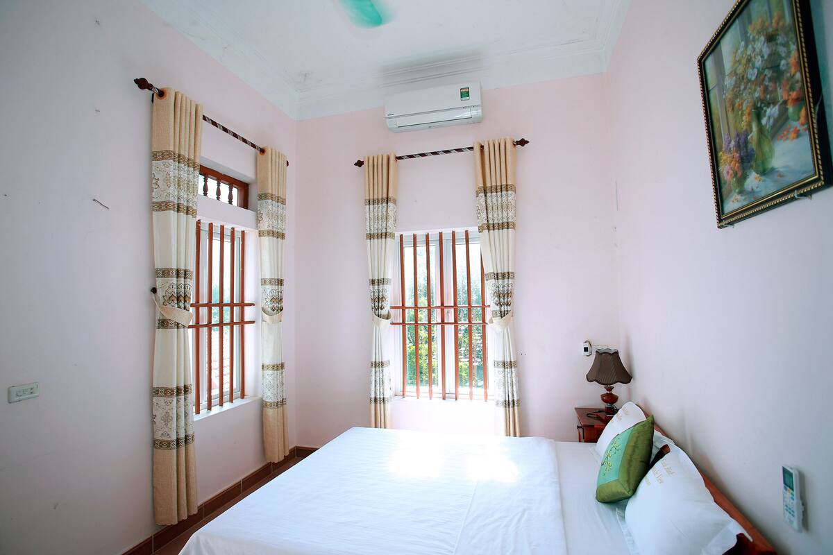 A room with a bed, a window with curtains, an air conditioning unit, a lamp, and a wall-mounted phone.