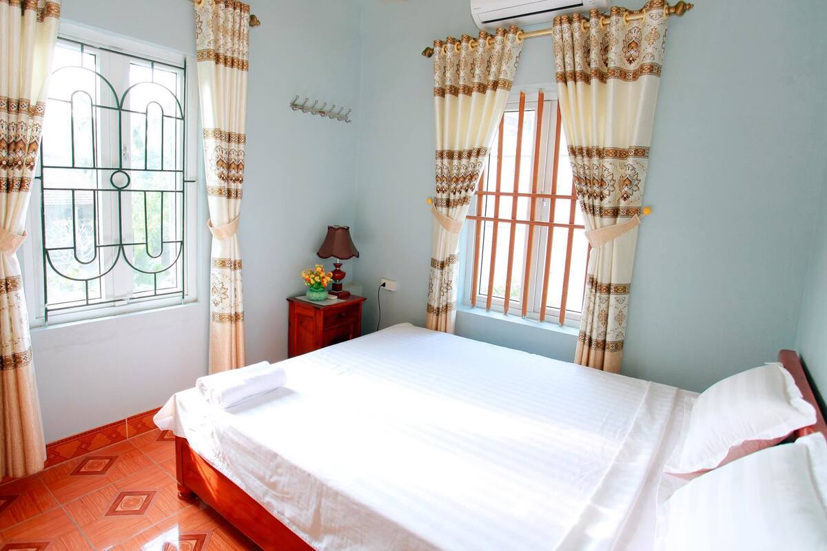 A bedroom with a bed, a nightstand with a lamp, and curtains on the windows.