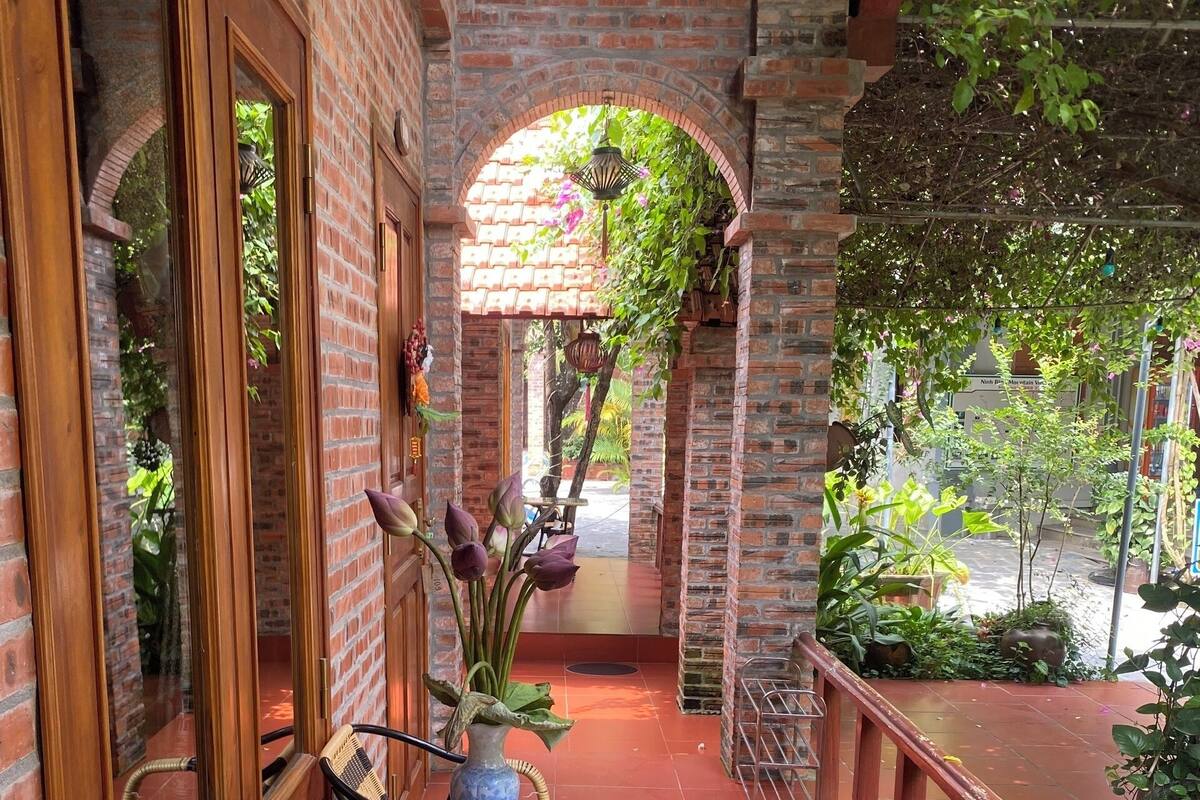 A covered outdoor seating area with brick walls, a glass table, wicker chairs, and potted plants.