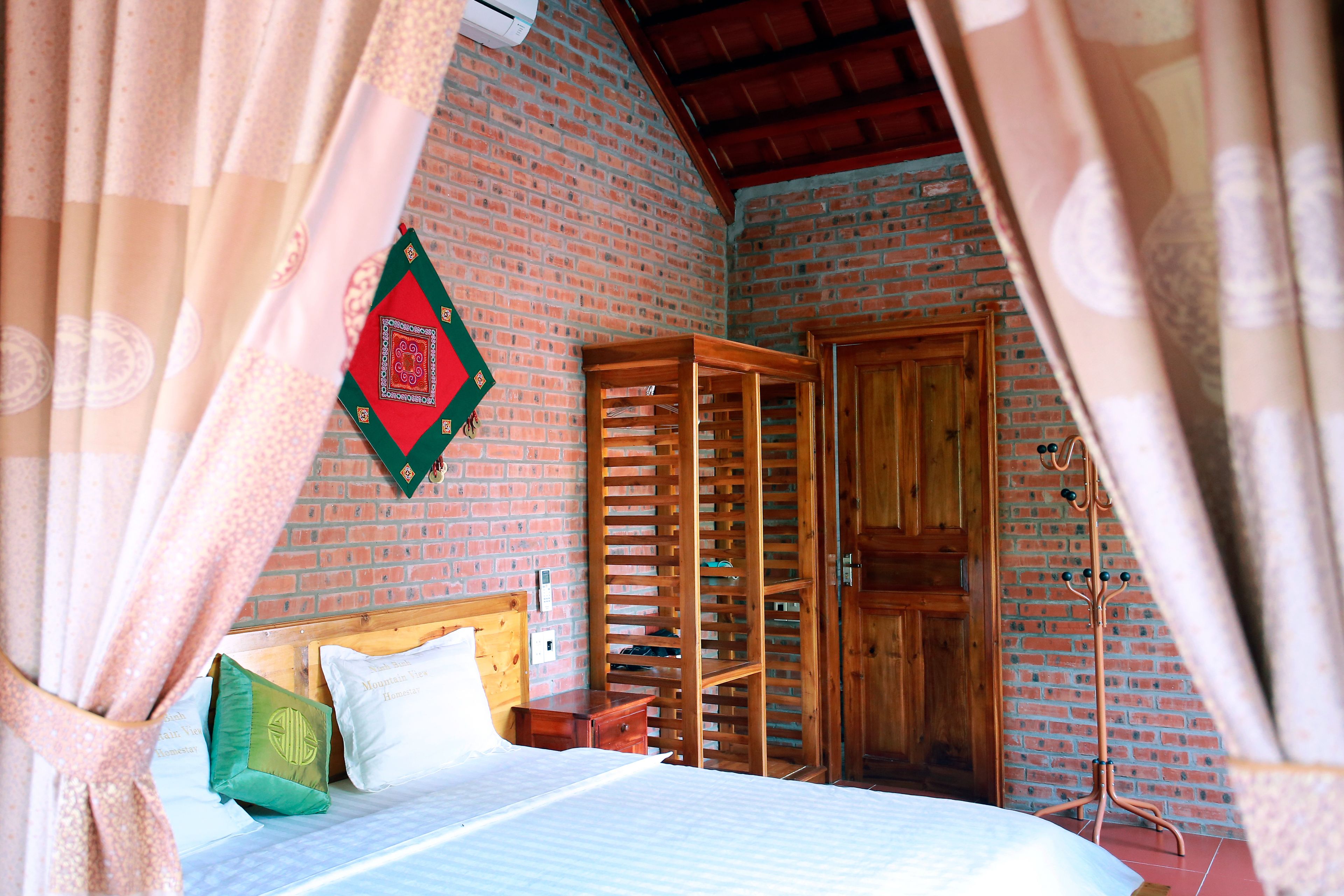 A bedroom with a bed, a wooden wardrobe, and a brick wall.
