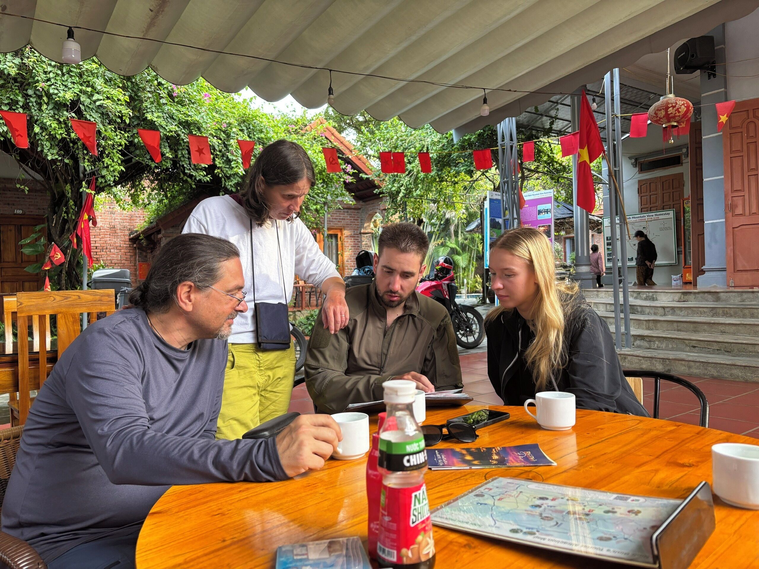 A group of people seated at a wooden table with a map and a bottle of soda.