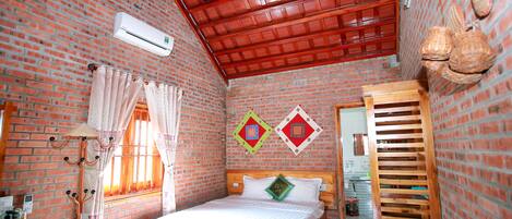 Una habitación con pared de ladrillo, una cama con ropa blanca, un ventilador de techo y una ventana con cortinas.