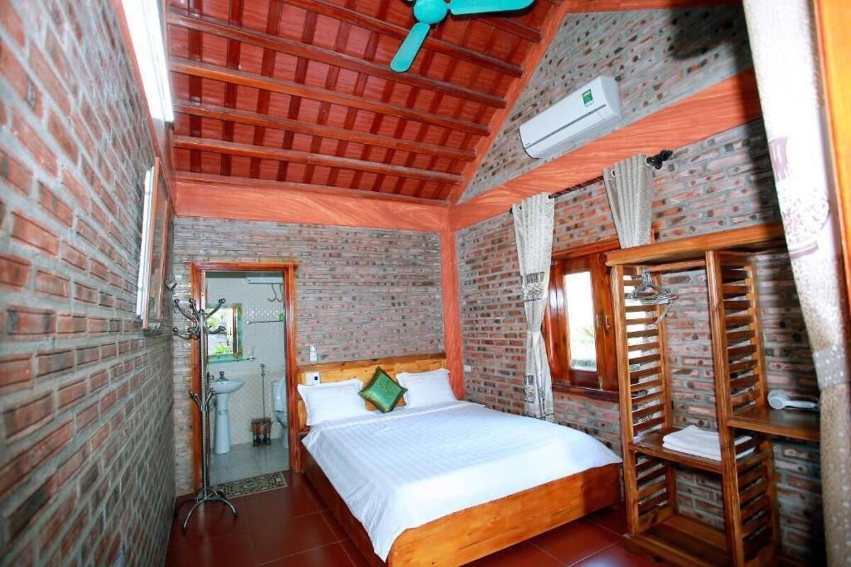 A room with a brick wall, a wooden bed, a ceiling fan, and a window.