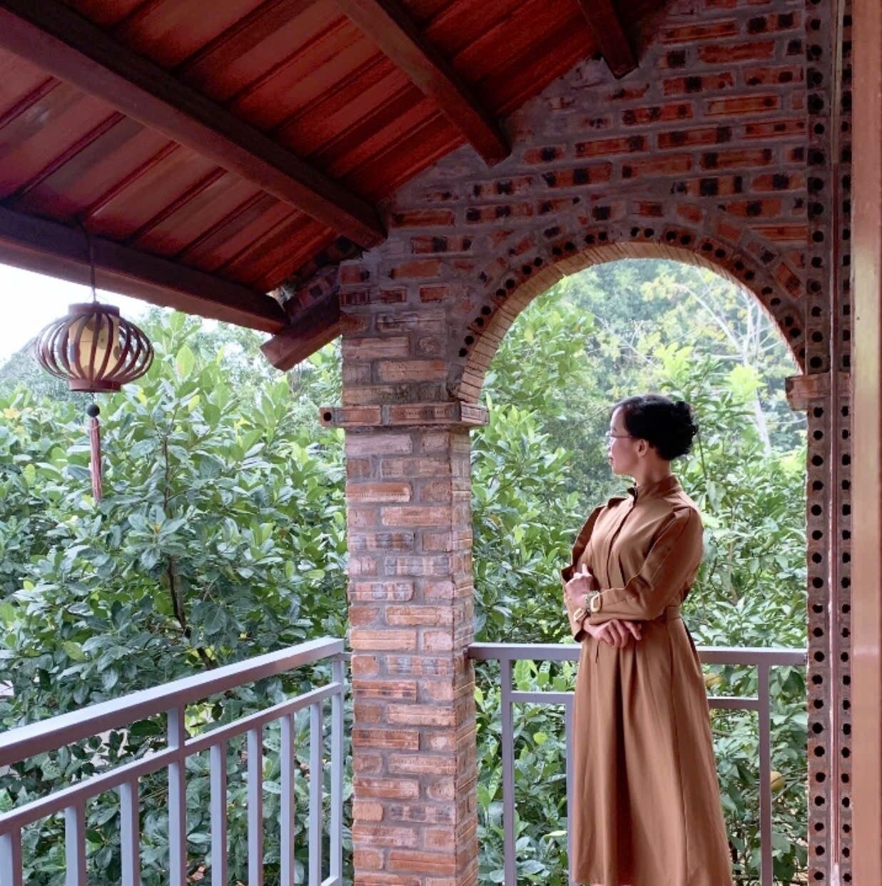 A person standing on a balcony with a brick archway, overlooking a lush green landscape.