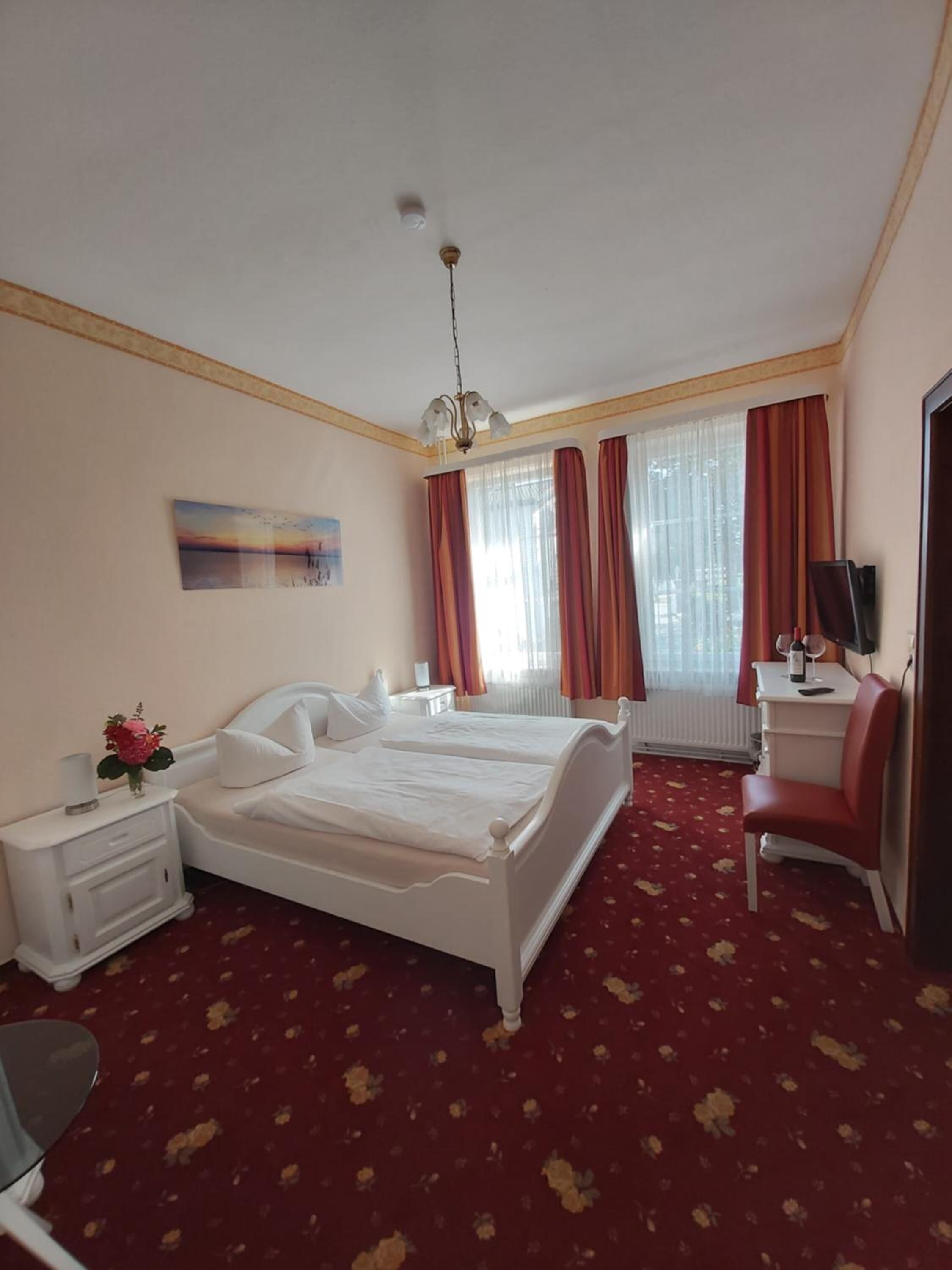Ein Hotelzimmer mit einem großen Bett, einem Schreibtisch, einem Sessel, einem Fernseher und einem Vorhangfenster.