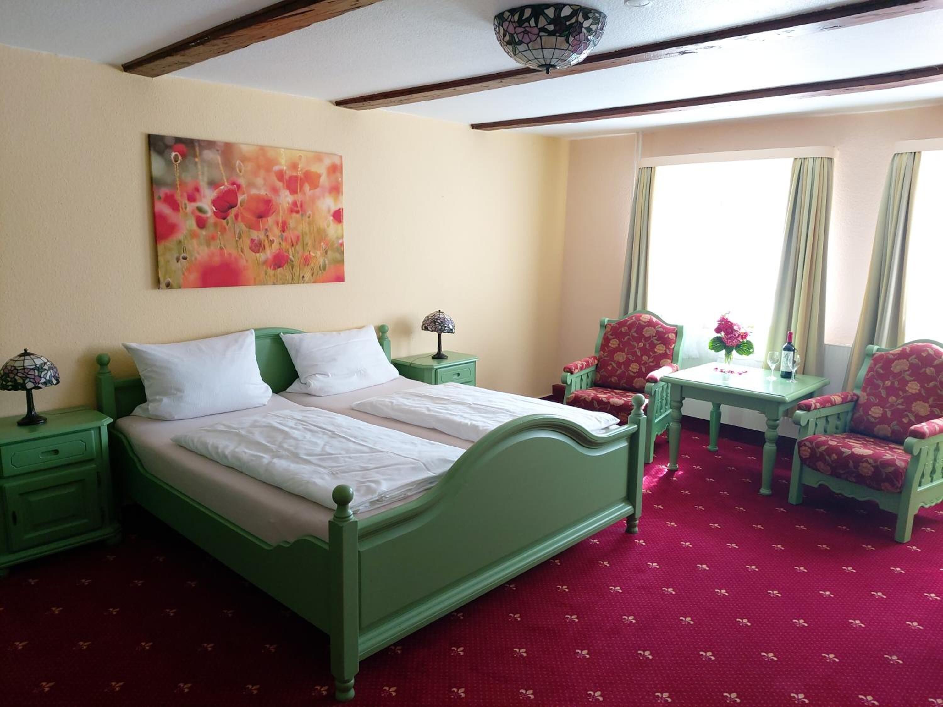 Una habitación con una cama verde, un escritorio, dos sillas y un cuadro en la pared.