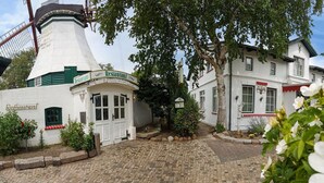 A traditional white building with a green door and windows, adjacent to a windmill. - Hotel Der Muehlenhof (Westerdeichstrich)
