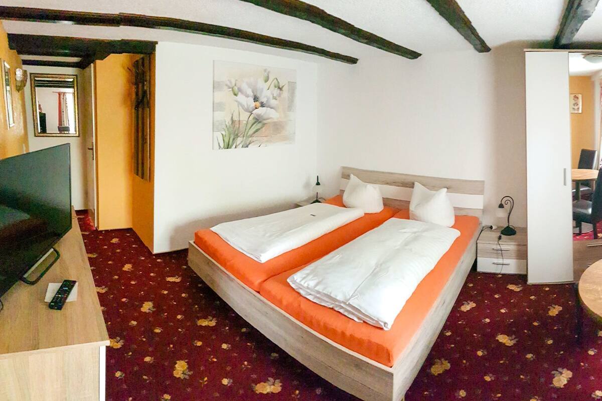 Una habitación con una cama, un escritorio, una silla, una mesa y un ventanal con cortinas.