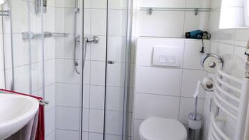 Et badeværelse med en glasafskærmet brusekabine, en hvid vask med et rødt håndklæde, et toilet og en håndklædestang.