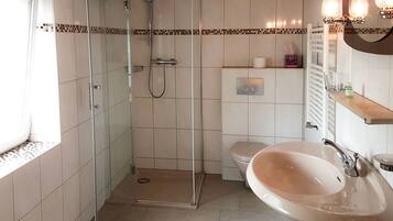 Un baño con ducha acristalada, inodoro y lavabo con espejo.