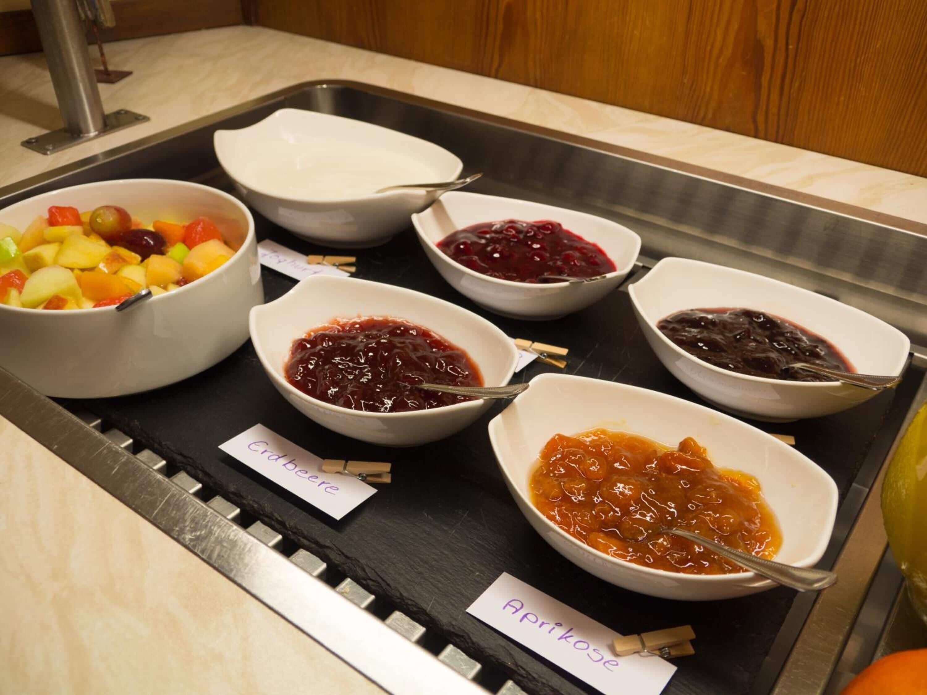 A buffet with various fruit and vegetable dishes, including labeled containers for different types of jams and pickles.
