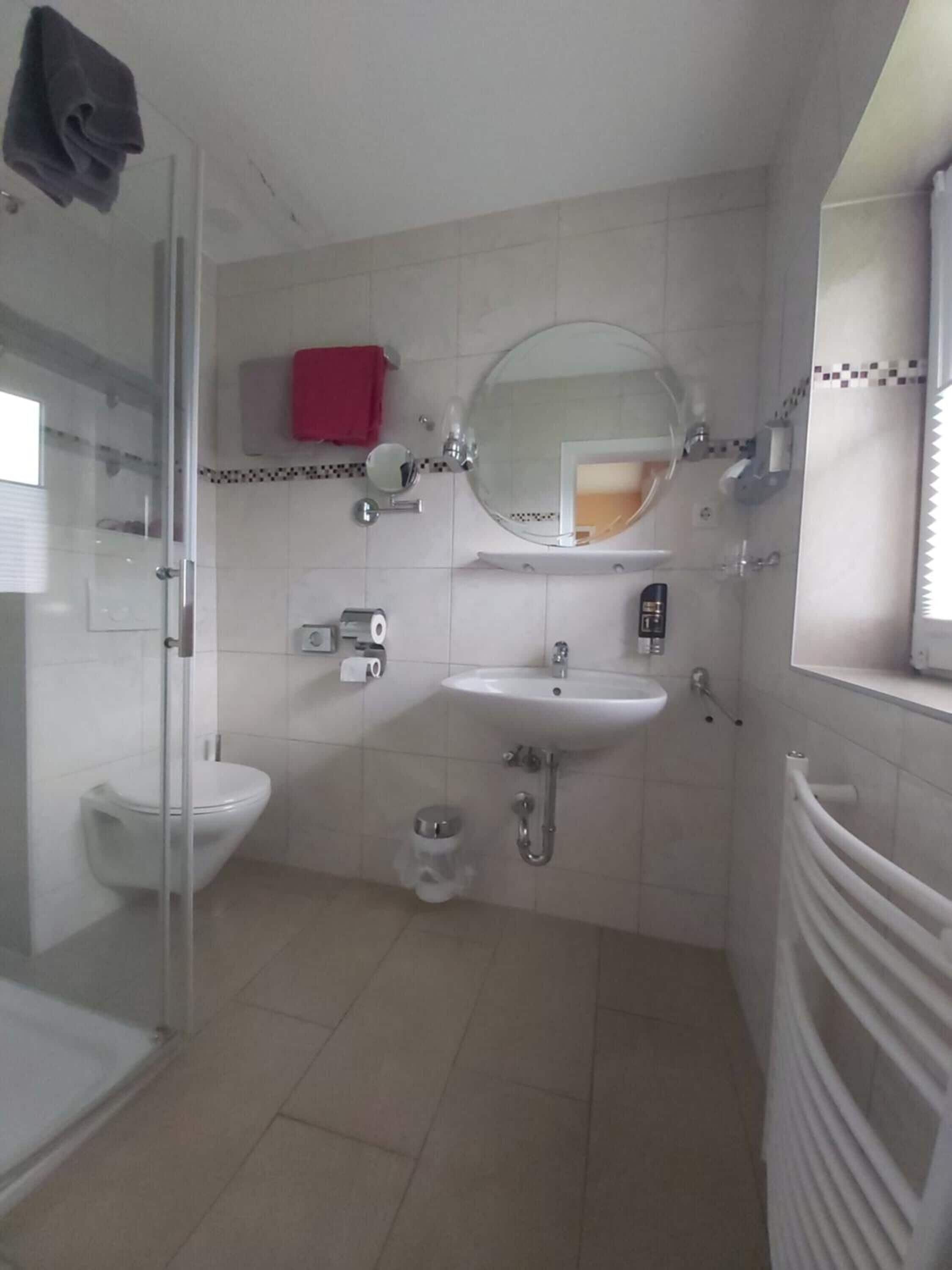 Ein Badezimmer mit Duschkabine aus Glas, einem weißen Waschbecken, einer Toilette und einem Handtuchhalter.
