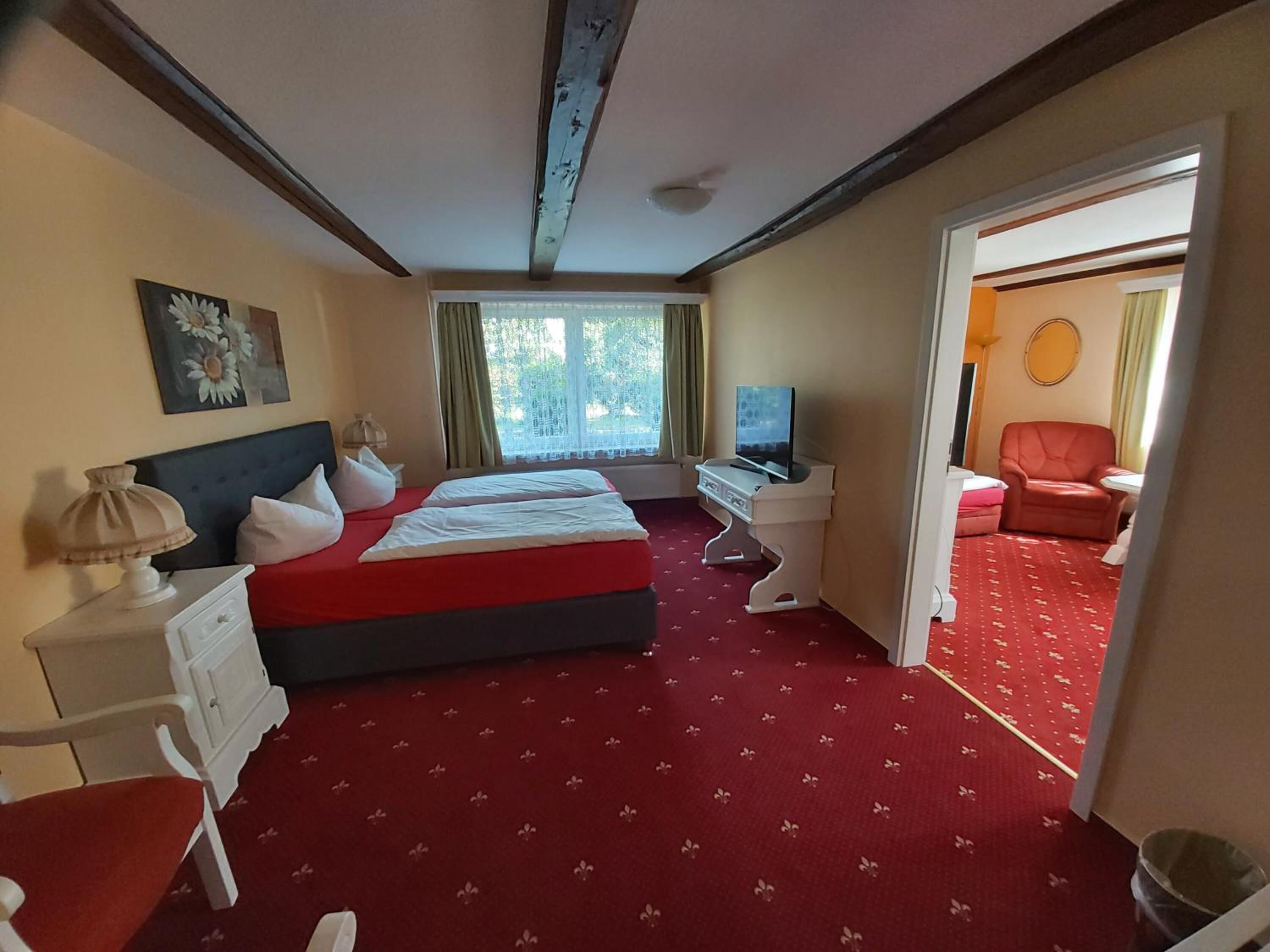 Une chambre d’hôtel avec un grand lit, un bureau, une télévision et une moquette rouge.