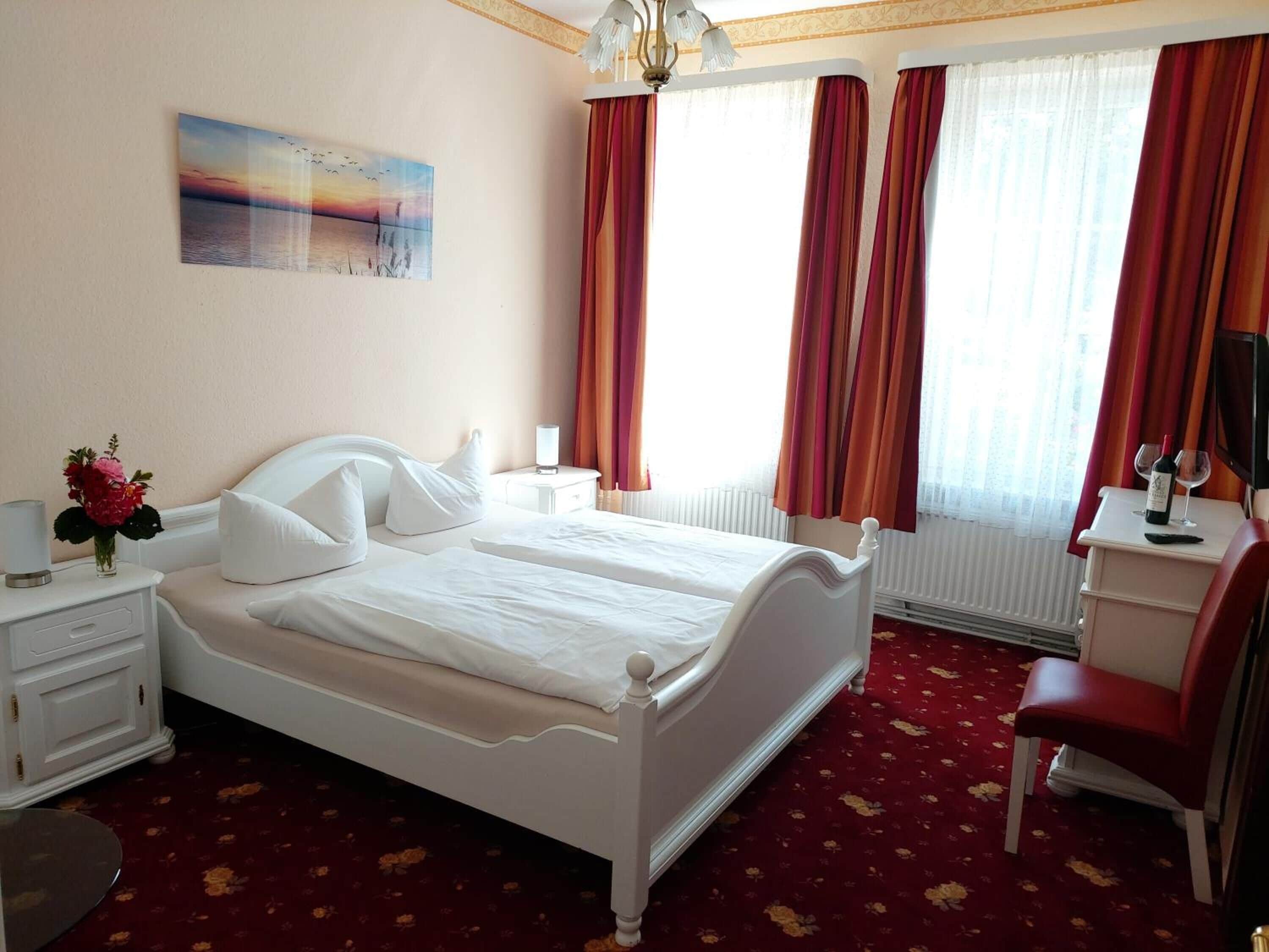 Ein Hotelzimmer mit einem Doppelbett, einem Schreibtisch mit Stuhl, einem Heizkörper und einem Bild an der Wand.