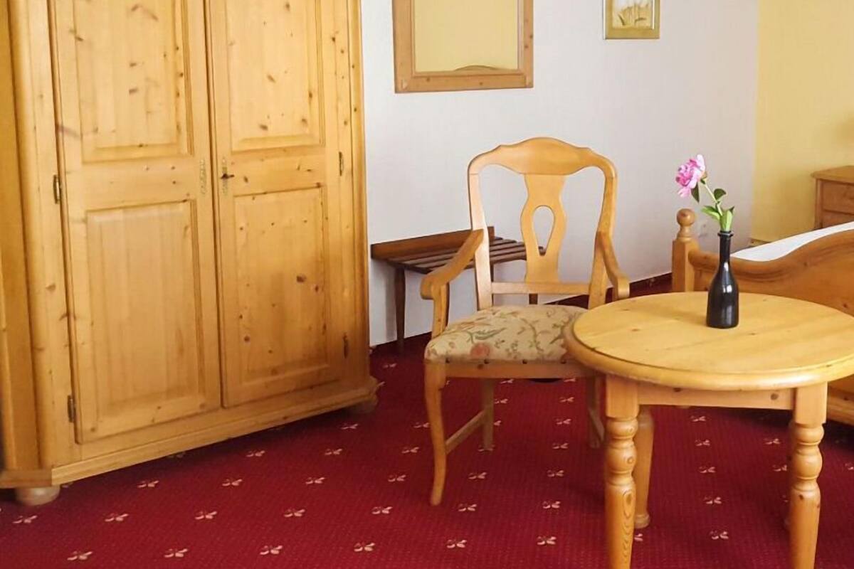 Una habitación con un armario de madera, una silla, una mesita con un jarrón y un espejo en la pared.