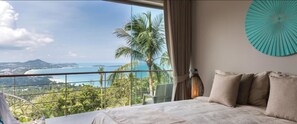 Enjoy a restful stay with a large bed overlooking a scenic coastal view of palm trees and water.