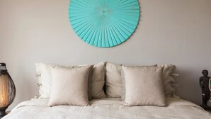 A bed with a beige headboard and two pillows, a wall-mounted circular blue artwork, a lamp, and a statue on the side. - Villa Nuéa at Comoon Boutique Villas (Koh Samui)