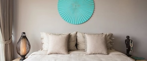 A bed with a beige headboard and two pillows, a wall-mounted circular blue artwork, a lamp, and a statue on the side. - Villa Nuéa at Comoon Boutique Villas (Koh Samui)