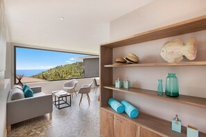 Relax in a serene coastal retreat with a large window offering breathtaking views, a comfortable sofa, and a stylish shelf unit.