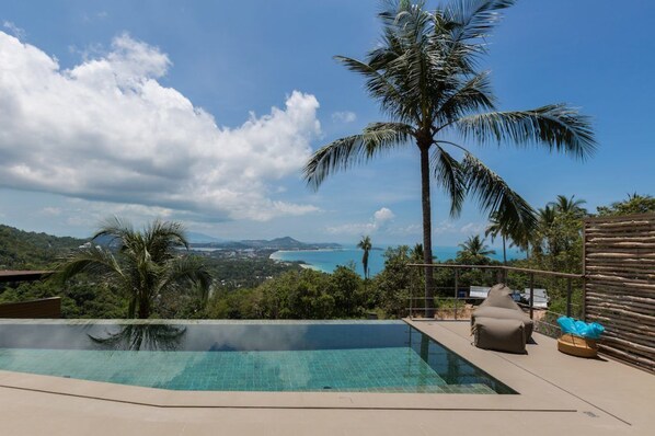 Relax by the infinity pool overlooking a serene coastal landscape with a tranquil beach and distant mountains.