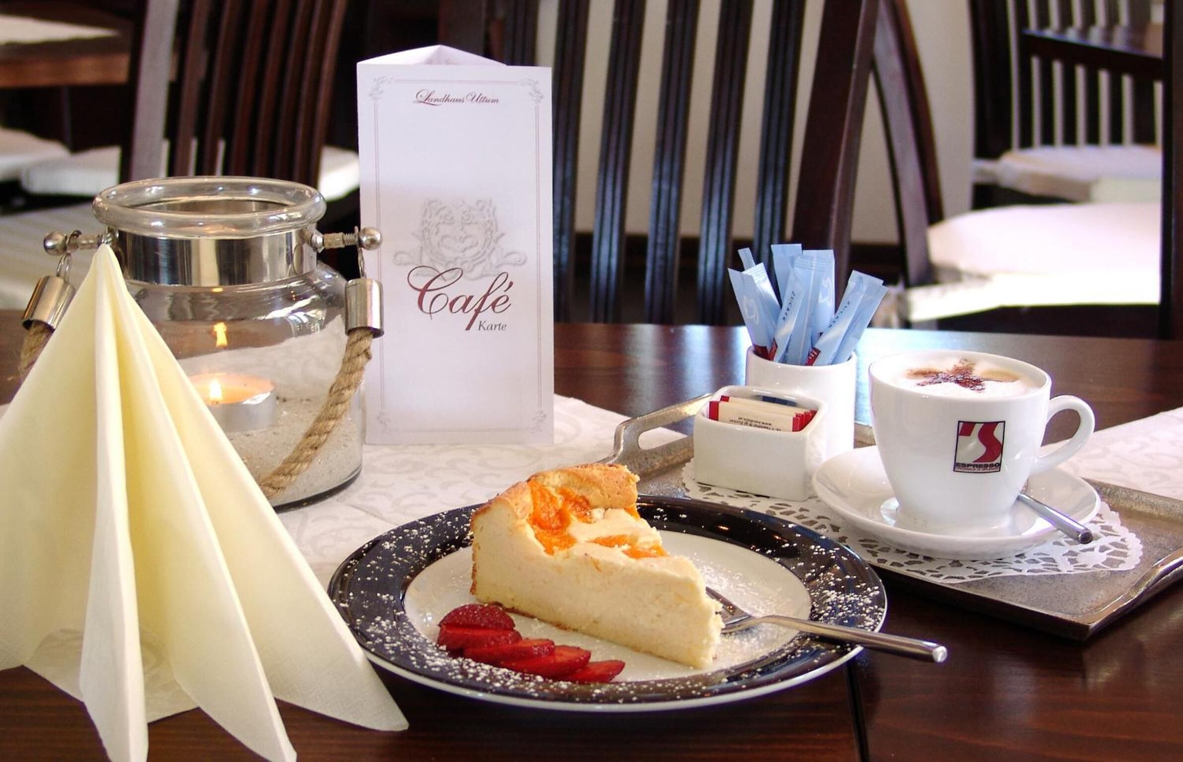 A table setting with a slice of cheesecake, a candle, a menu, and a cup of coffee.