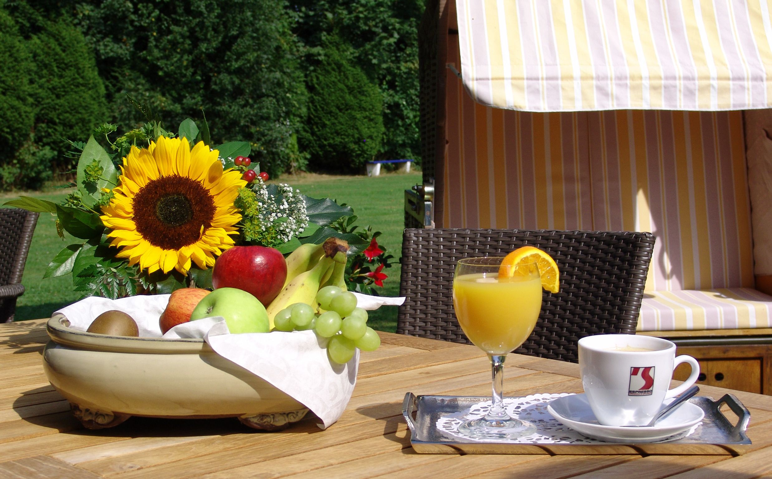 Una mesa con un frutero, un vaso de jugo de naranja y una taza de café.