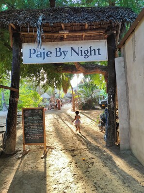 A rustic thatched-roof structure labeled "Paje By Night" with a signboard detailing sound healing and meditation services. - Paje By Night (Paje)