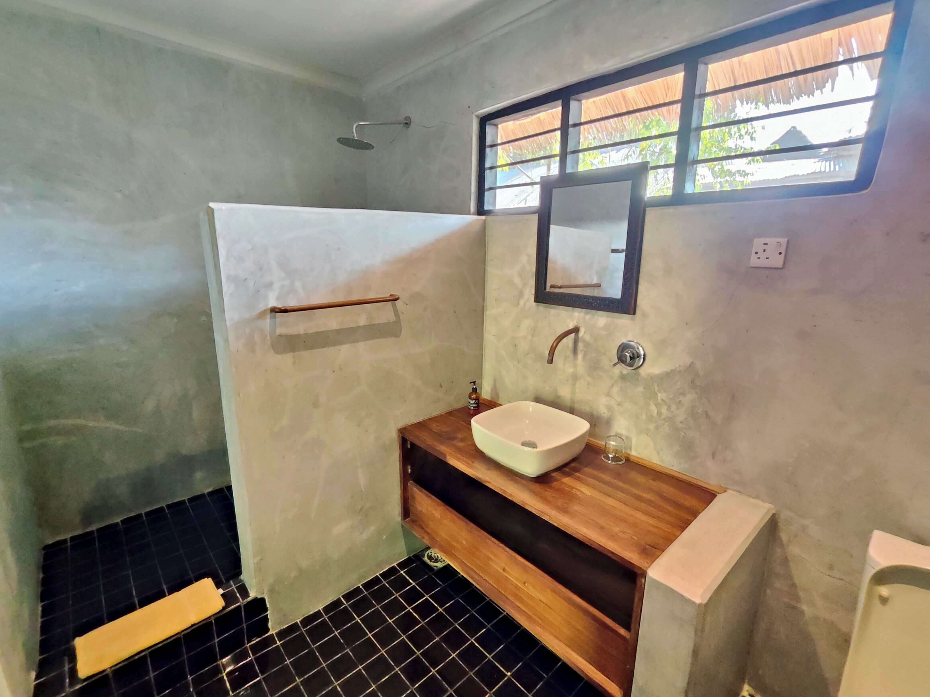 A bathroom with a white sink, wooden vanity, a towel rack, a shower, and a window with a view.