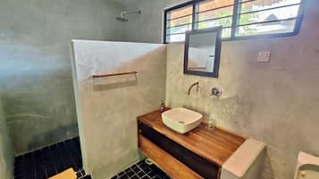 A bathroom with a white sink, wooden vanity, a towel rack, a shower, and a window with a view.