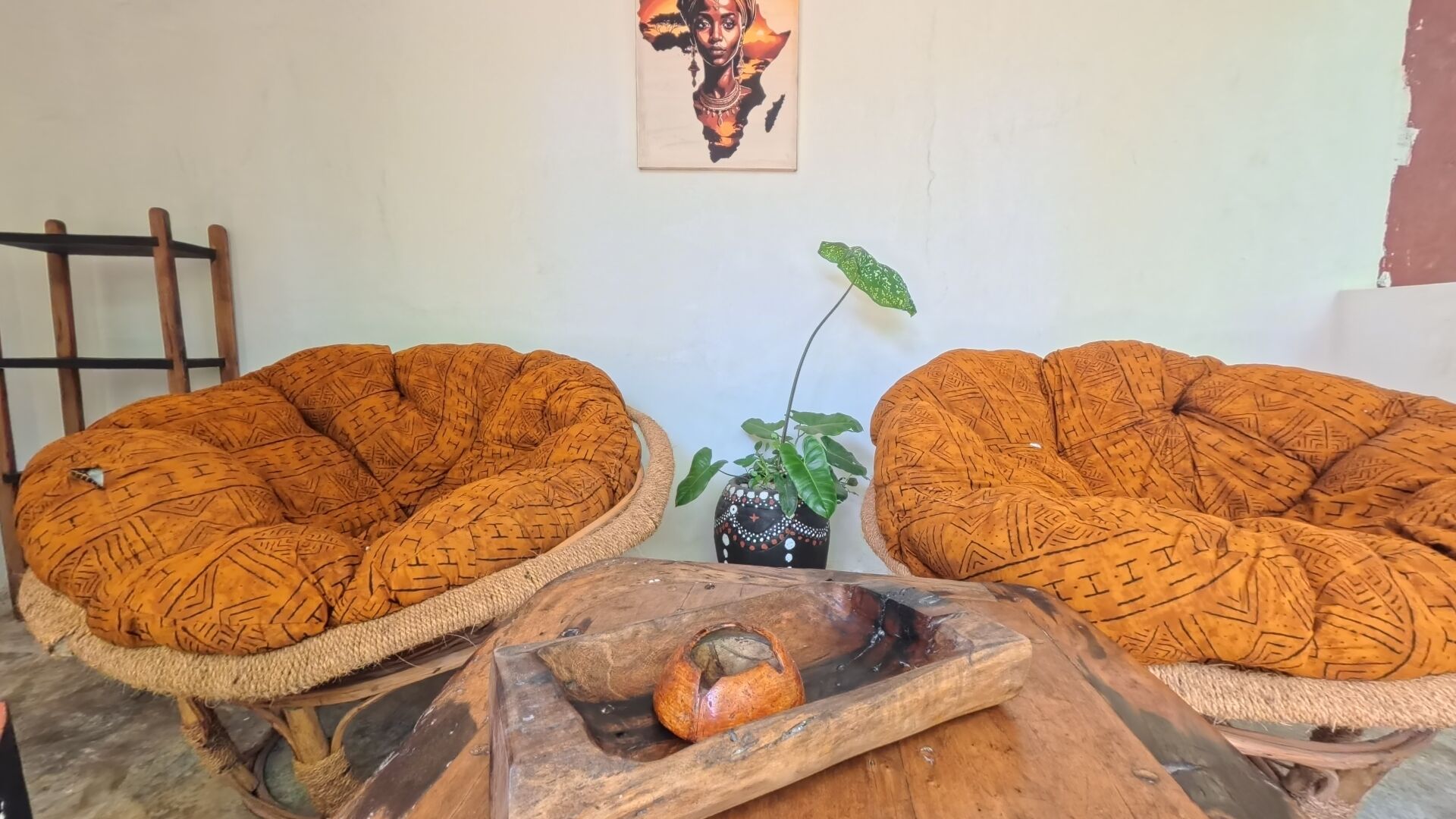 Dos sillones trenzados con motivos geométricos, una planta pequeña en maceta y una mesa de madera con una concha.