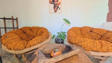 Dos sillones trenzados con motivos geométricos, una planta pequeña en maceta y una mesa de madera con una concha.