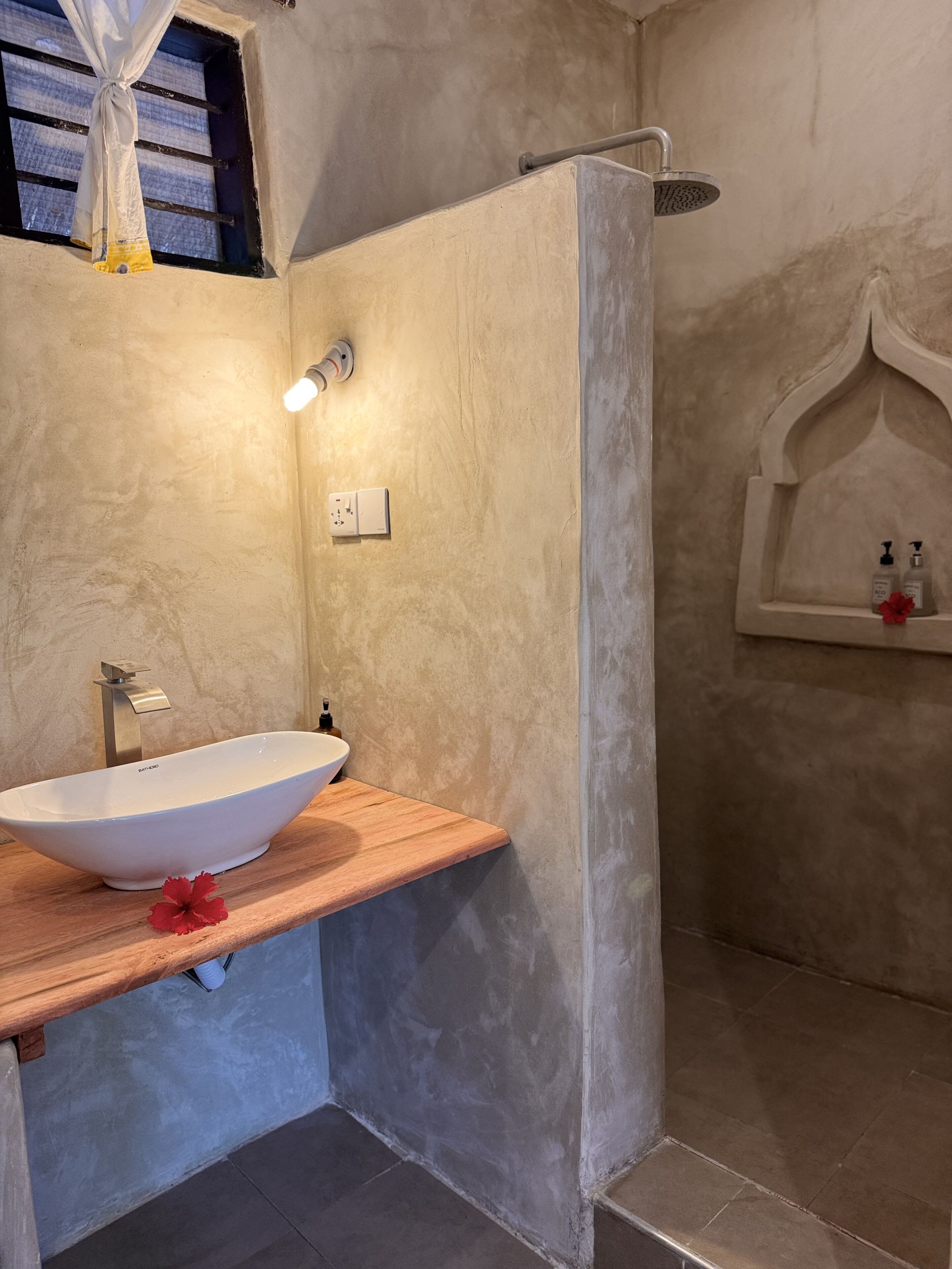 A bathroom with a freestanding bathtub, a showerhead, a wall-mounted light, and a shelf with toiletries.