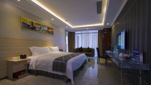 Una habitación de hotel moderna con una cama grande, una zona de estar con sofá, un escritorio con computadora y un televisor.