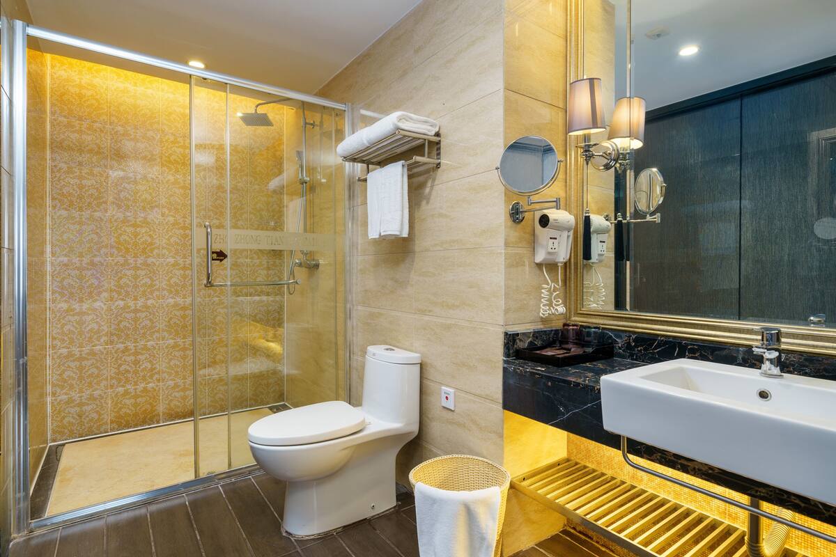 Ein modernes Badezimmer mit einer gläsernen Duschkabine, einer weißen Toilette, einem Waschbecken mit Marmorplatte und einem Spiegel mit Wandleuchten.